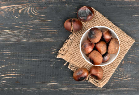 Roasted chestnuts in a white bowl on sacking empty wooden background, top view