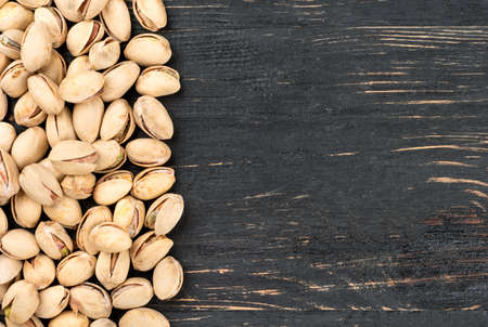 Scattered pistachio nuts on a blank wooden background