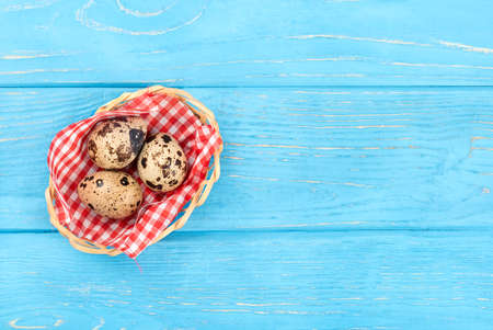 Three fresh quail eggs in a basket on an empty wooden background, top view