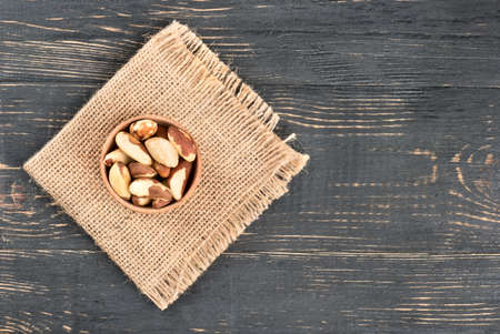 Small bowl filled with Brazil nuts on sackcloth and empty wooden background, top viewの写真素材