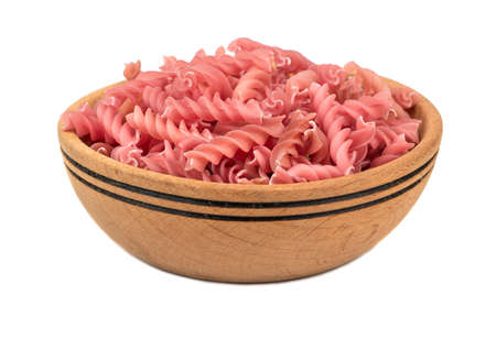 Red raw pasta fusilli in a wooden bowl on a white backgroundの写真素材