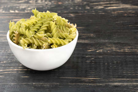 White bowl with raw pasta fusilli on wooden backgroundの写真素材