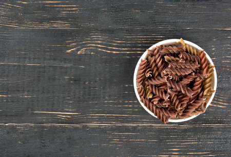 Dark pasta fusilli in a bowl on an empty table, top viewの写真素材