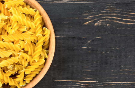Part of the bowls filled with raw pasta fusilli on wooden background, top viewの写真素材
