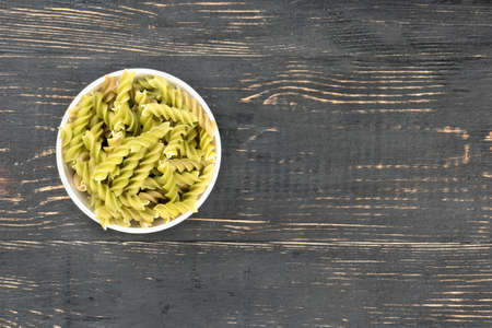 White bowl with raw pasta fusilli on wooden background, top viewの写真素材