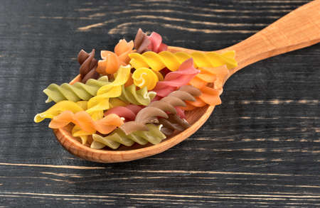 Colorful fusilli pasta in spoon on wooden background close-upの写真素材