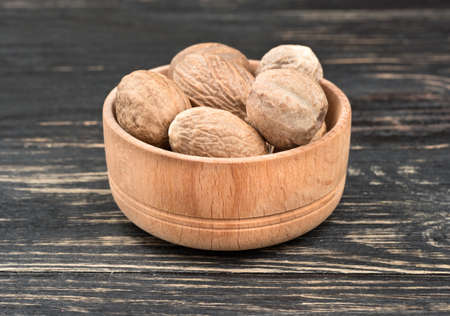 Dry nutmeg in the bowl on wooden background closeup
