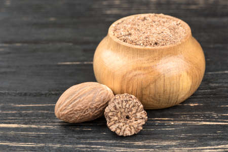 Jar with nutmeg powder and nuts on wooden background