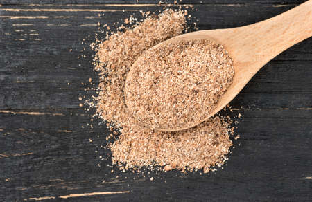 Nutmeg powder in spoon on wooden background, top view