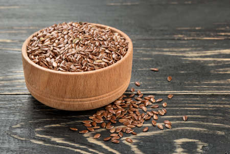 Flax seeds in bowl with scattered grains on dark wooden backgroundの写真素材