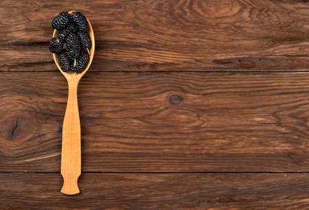 Spoon with fresh black mulberries on an empty wooden backgroundの写真素材