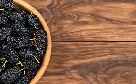 Part of bowl of fresh black mulberries on a wooden background, top viewの写真素材