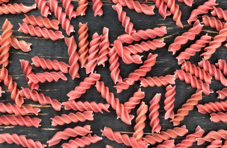 Scattered red pasta fusilli on wooden background, top view