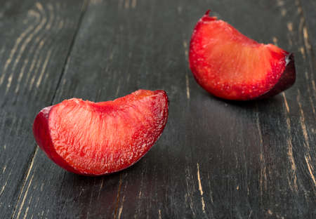 Two juicy slices of red plums on wooden background closeupの写真素材