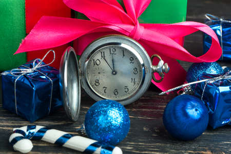 Christmas gifts and balls scattered on a table with an old clock