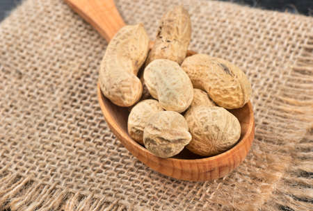 Wooden spoon with peanuts in the shell on sackcloth close up