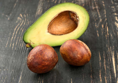 Two seeds avocado with half on wooden background