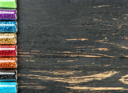 Few bottles of sparkles for the design of nails and makeup on an empty wooden background