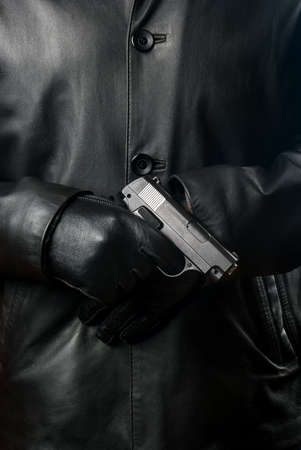 Bandit in a black jacket with gloves and a gun close-upの写真素材