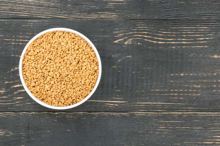Ceramic bowl with grains of fenugreek on an empty wooden background, top viewの写真素材