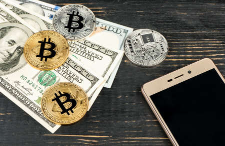 Gold and silver bitcoin coins with dollars and smartphone on wooden backgroundの写真素材