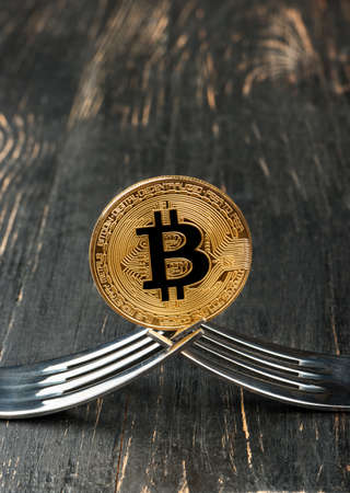 Gold bitcoin coin with two forks on wooden backgroundの写真素材
