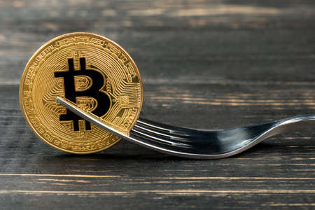 Gold bitcoin coin with fork on wooden backgroundの写真素材
