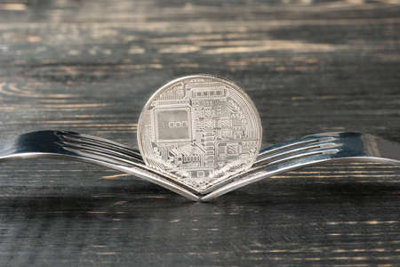 Silver bitcoin coin with two forks on wooden backgroundの写真素材