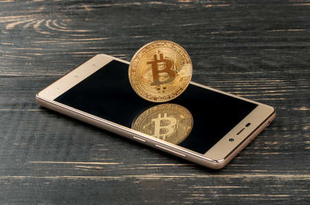 Gold bitcoin coin on smartphone on wooden backgroundの写真素材