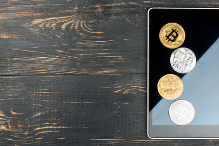 Tablet with silver and gold bitcoin coins on empty wooden backgroundの写真素材