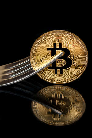 Gold bitcoin coin with fork on black backgroundの写真素材