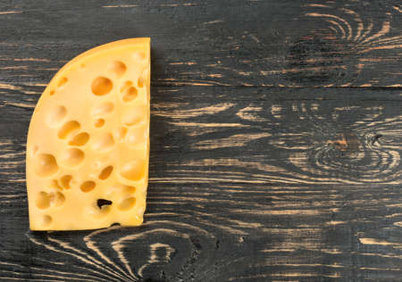 Piece of cheese with holes on a blank wooden background, top viewの写真素材