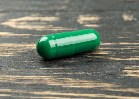 Green herbal capsule on wooden background closeup