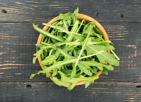 Green arugula leaves in bowl on wooden background, top viewの写真素材