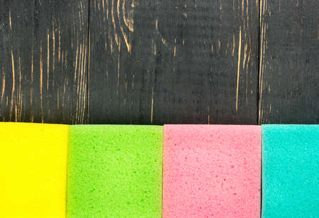 Three colored sponges for washing dishes on a wooden background, top view