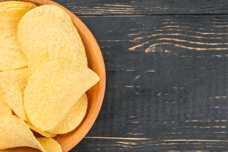 Part of bowl with potato chips on empty wooden background