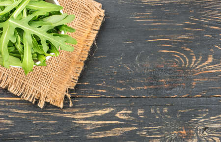 Part of bowl with arugula leaves on burlap and blank wooden backgroundの写真素材