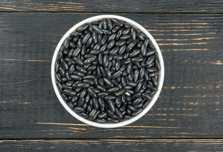 Bowl with black beans on a wooden background, top view