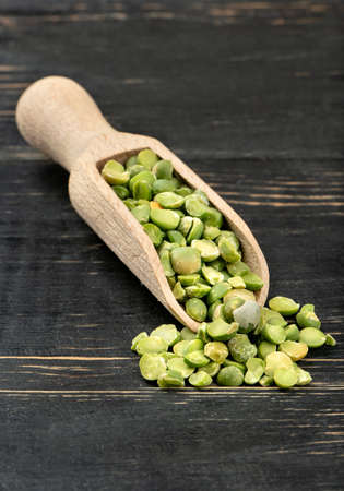 Dry green peas in scoop on wooden background closeup