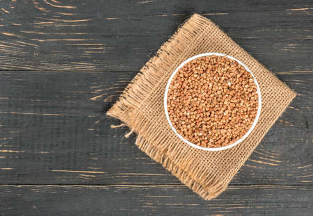 White bowl with raw buckwheat on burlap and empty wooden backgroundの写真素材