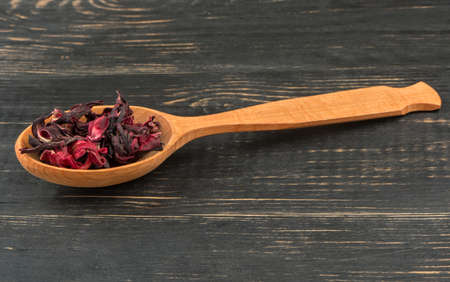 Dry karkade tea in a spoon on wooden background closeupの写真素材