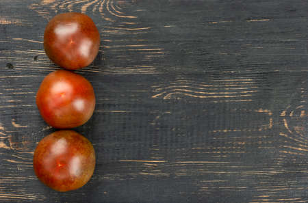 Three fresh kumato tomatoes on empty wooden backgroundの写真素材