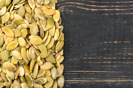 Scattered pumpkin seeds without shell on empty wooden background