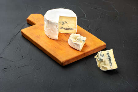 Brie cheese with two slices on cutting board on dark wooden backgroundの写真素材