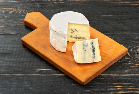Brie cheese with slice on cutting board and wooden backgroundの写真素材