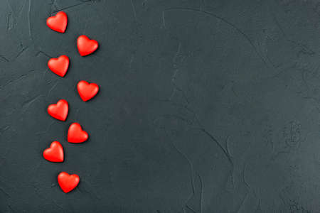 Scattered red plastic hearts on empty dark background, top view