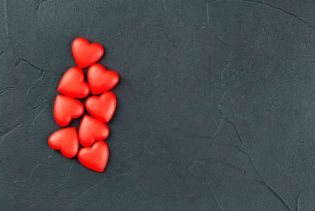 Scattered red plastic hearts on empty dark background, top viewの写真素材