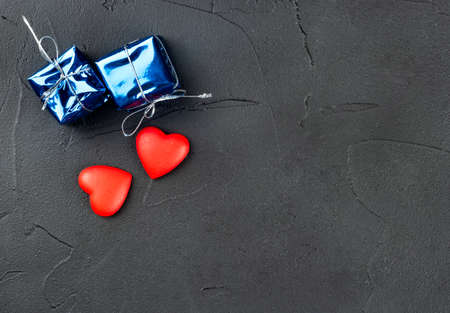 Two hearts with a gift on a dark background, top view