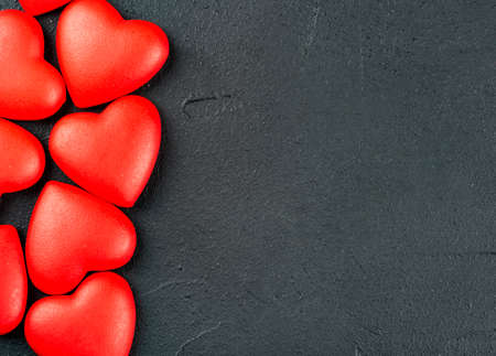 Scattered red plastic hearts on dark background closeup, top viewの写真素材
