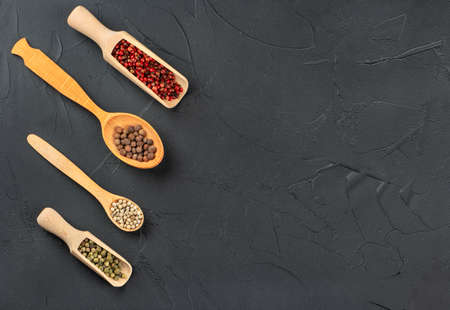 Mixtures of different peppers in spoons on a concrete background